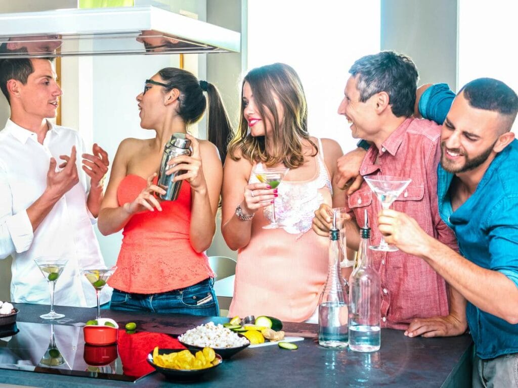 A group of five people enjoying drinks and snacks around a kitchen counter.