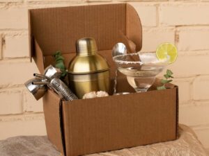 Cardboard box containing a cocktail shaker, jigger, strainer, margarita glass with lime, and a cork.