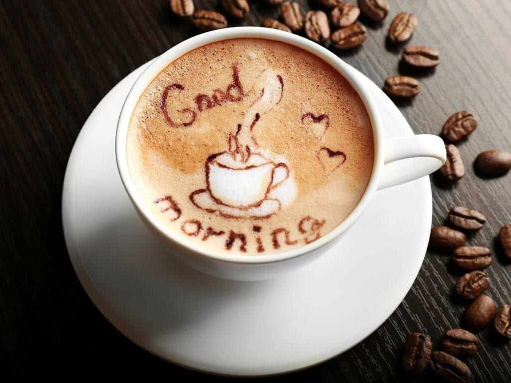 A cup of coffee with latte art showing a steaming cup and the words "Good morning,".