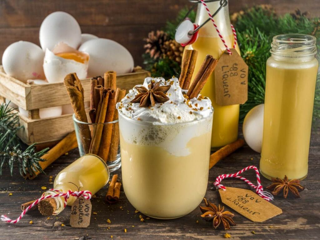 A glass of eggnog with whipped cream and star anise sits on a wooden table.