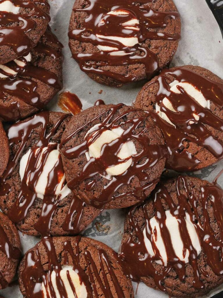 Chocolate cookies with marshmallows on top, drizzled with chocolate sauce.