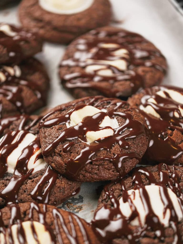 Chocolate cookies with a dollop of cream and drizzled chocolate, arranged on a baking sheet.