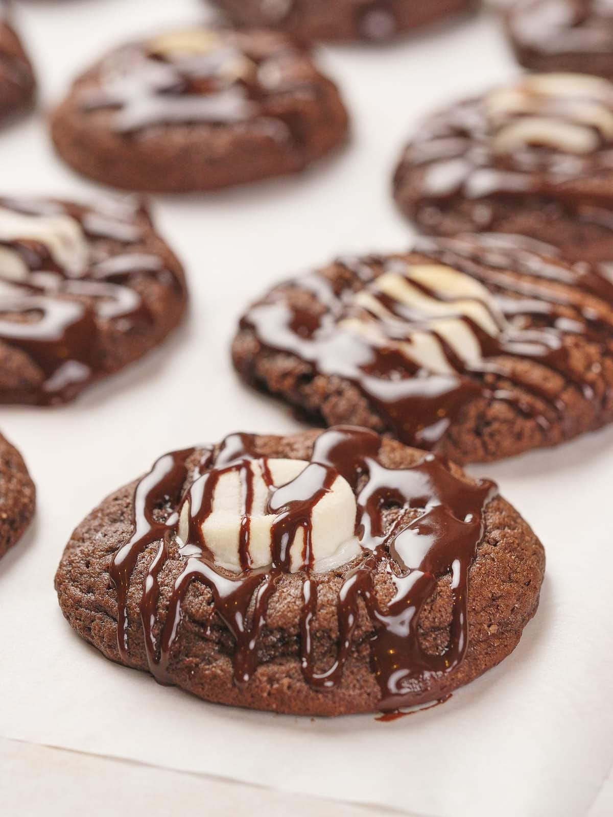 Chocolate cookies with white chocolate centers and drizzled chocolate on top, arranged on parchment paper.