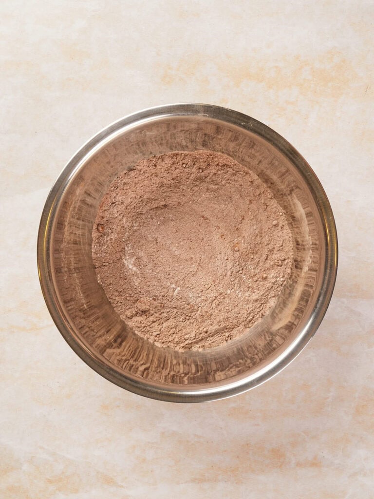 A metal bowl filled with a light brown, powdery substance sits on a light-colored surface.