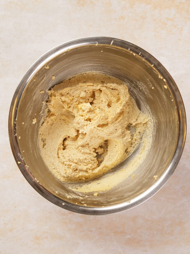 A metal mixing bowl containing a smooth, light brown cookie dough mixture.