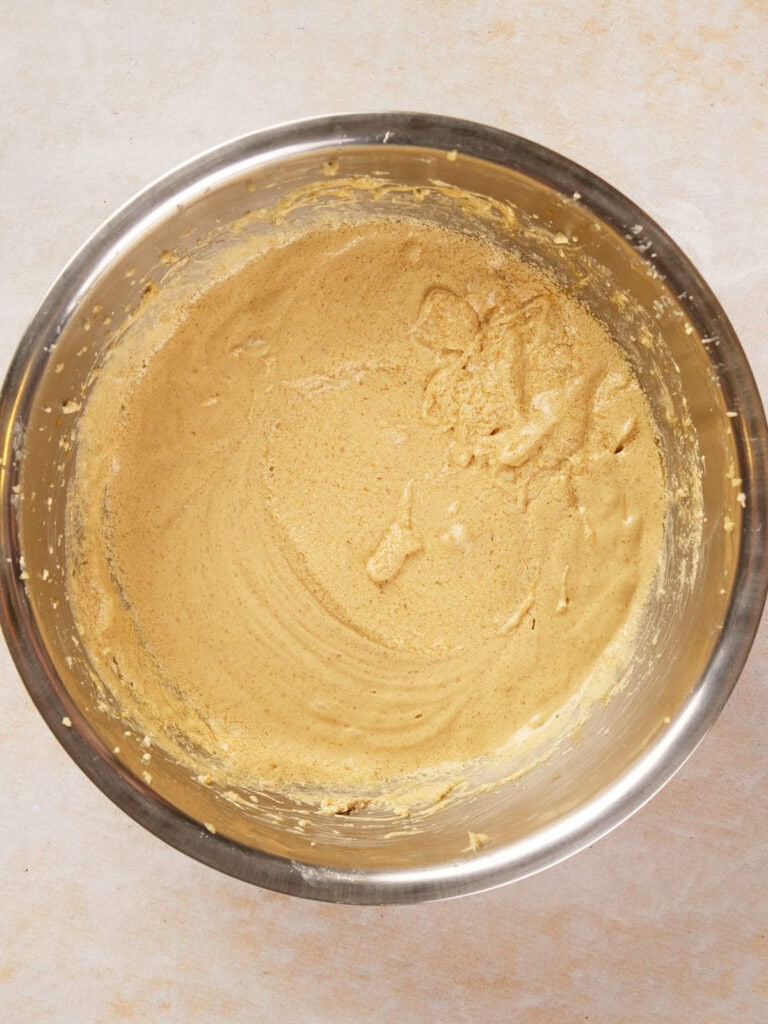 A metal bowl containing smooth, light brown batter on a light countertop.