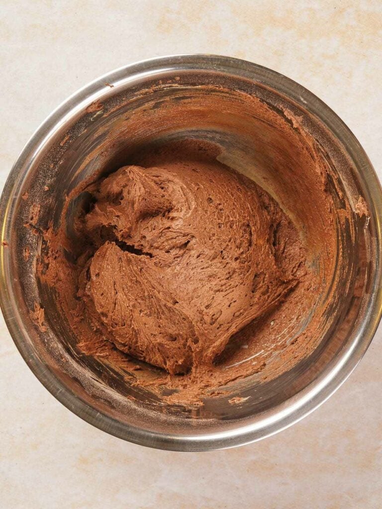 A stainless steel bowl filled with chocolate cake batter on a light-colored surface.