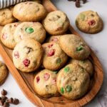 Wooden platter with M&M cookies for Christmas containing red and green candies and chocolate chips, placed on a marble surface with chocolate chips.