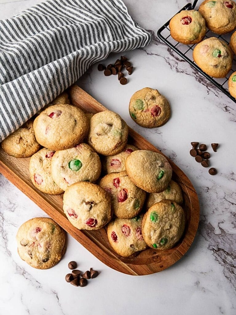 A wooden tray and wire rack hold M&M cookies for Christmas with red and green candies.