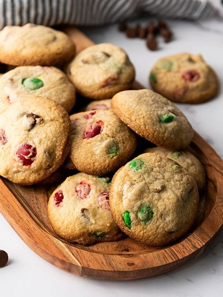 A wooden platter with M&M cookies for Christmas featuring red and green candy pieces.