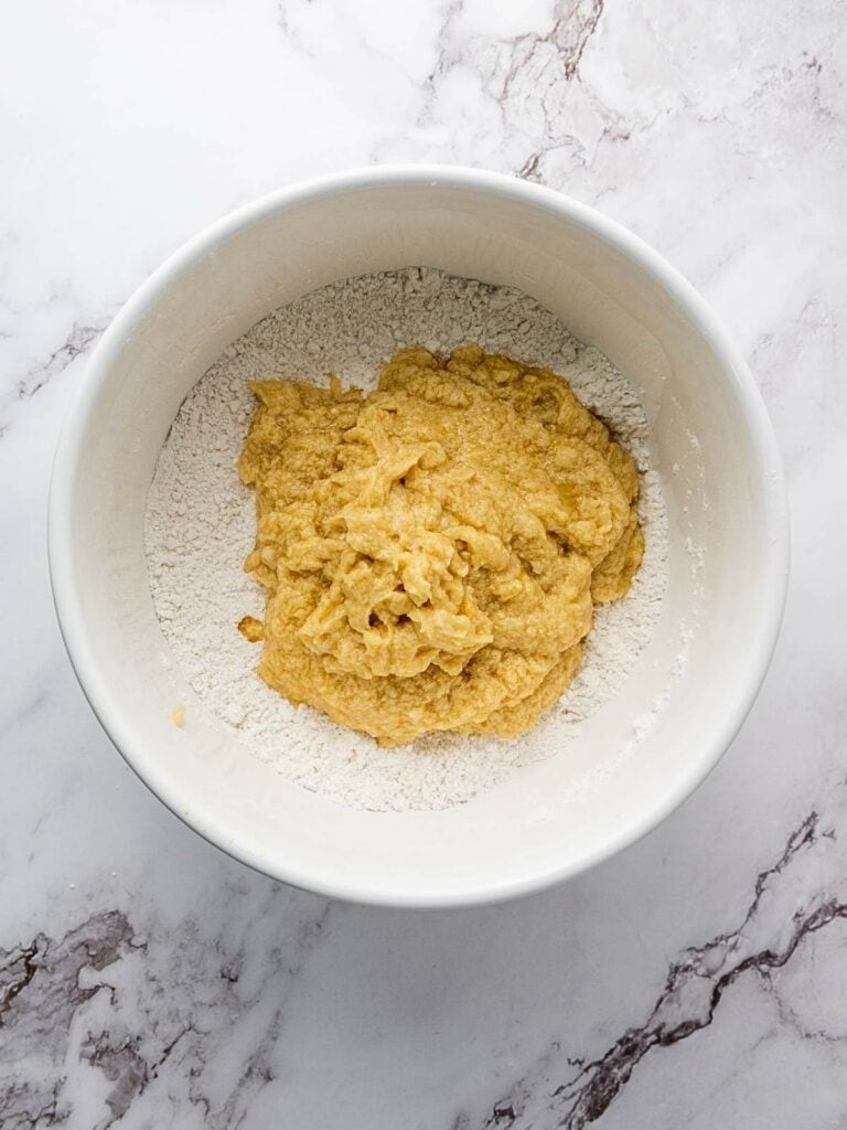 A mixing bowl with dough on top of dry flour on a marble countertop.