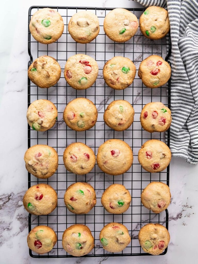 A cooling rack with 24 freshly baked cookies dotted with red and green candies.