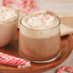 A glass of peppermint mocha topped with whipped cream on a wooden tray.