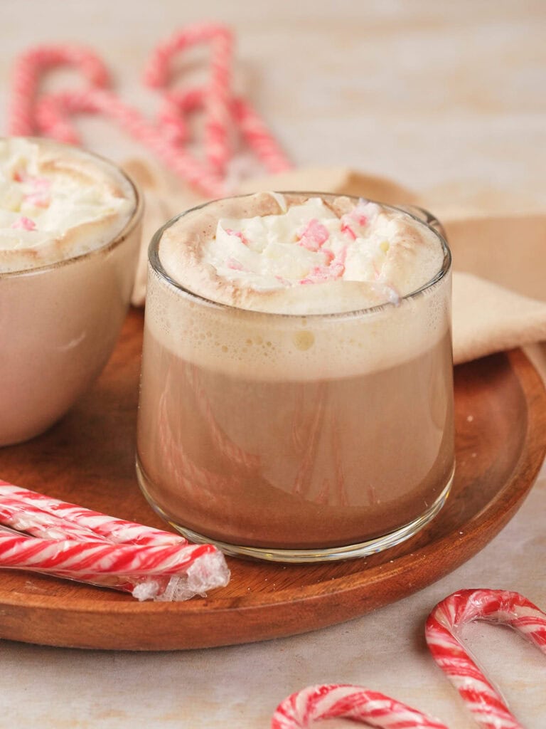 A glass of peppermint mocha topped with whipped cream on a wooden tray.