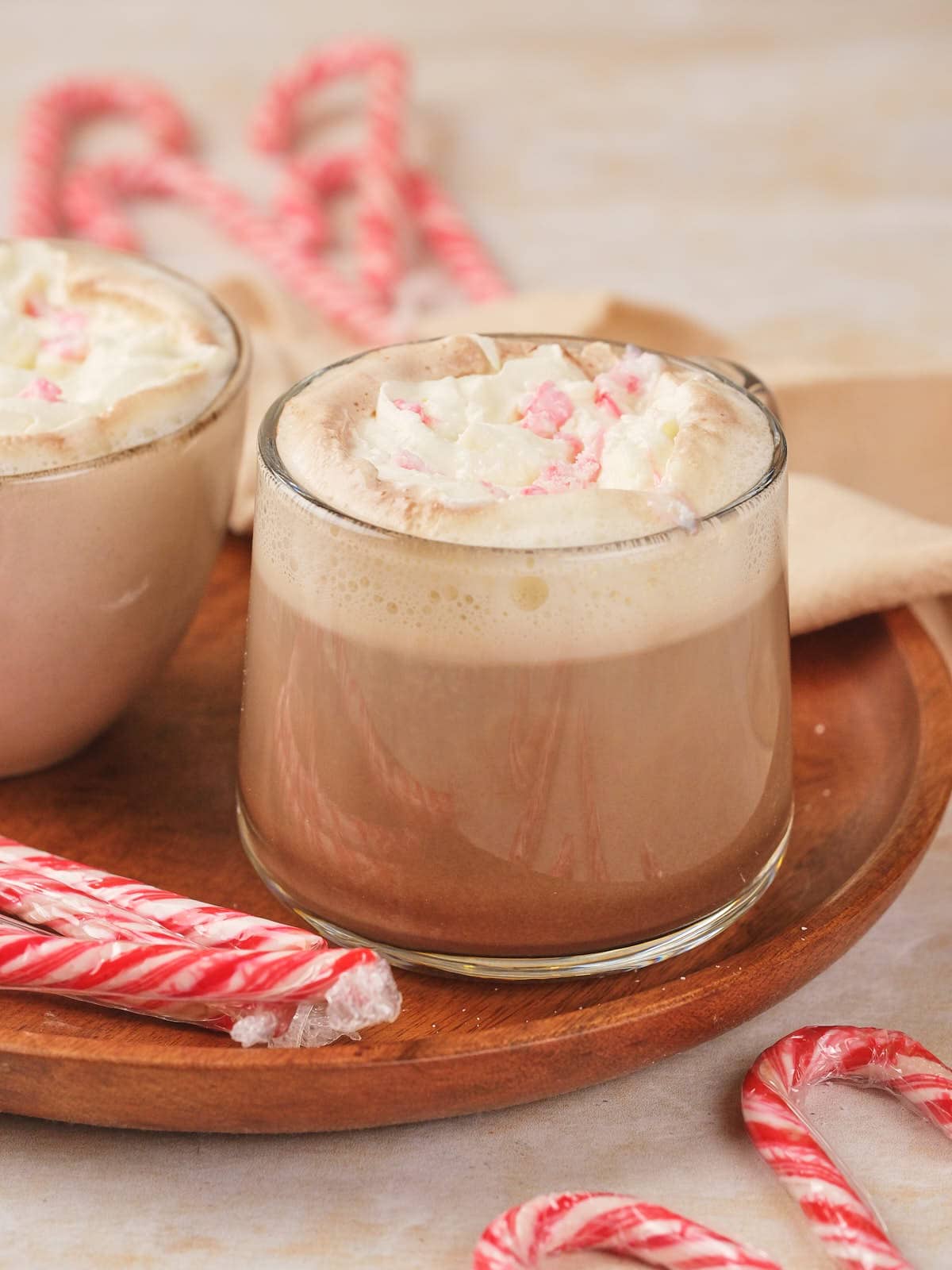 A glass of peppermint mocha topped with whipped cream on a wooden tray.