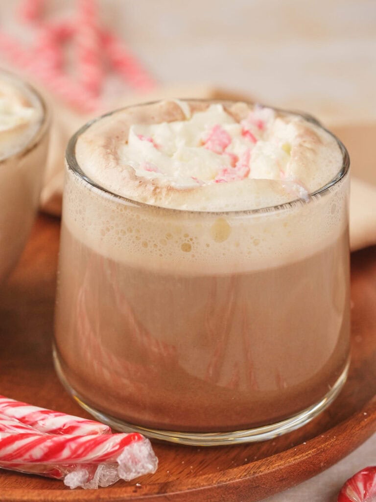 A glass of peppermint mocha topped with whipped cream, placed on a wooden tray.