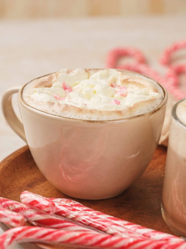 A mug of peppermint mocha topped with whipped cream sits on a wooden plate next to several candy canes.