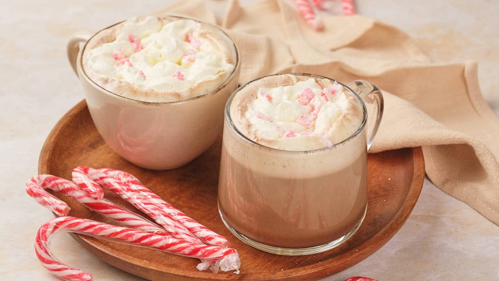 Two mugs of peppermint mocha topped with whipped cream and crushed candy canes.