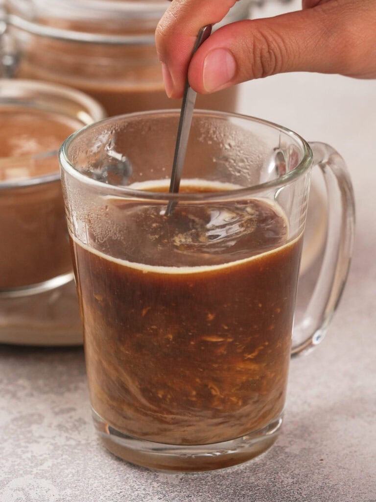 A hand stirring a glass mug filled with peppermint mocha coffee creamer.