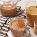 Jars and glasses filled with peppermint mocha coffee creamer, set on a striped cloth and tray.