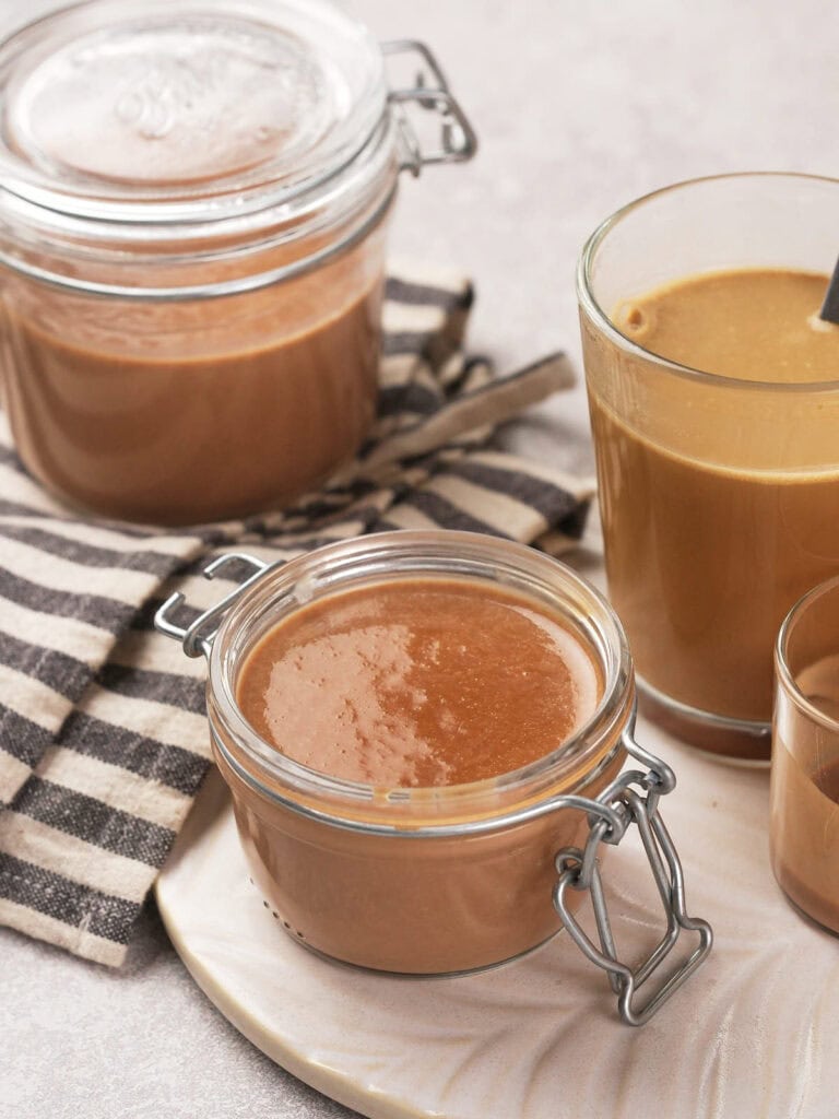 Jars and glasses filled with peppermint mocha coffee creamer, set on a striped cloth and tray.