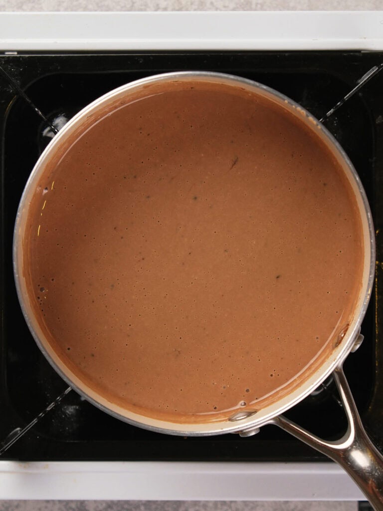 A saucepan filled with smooth brown gravy on a stovetop.