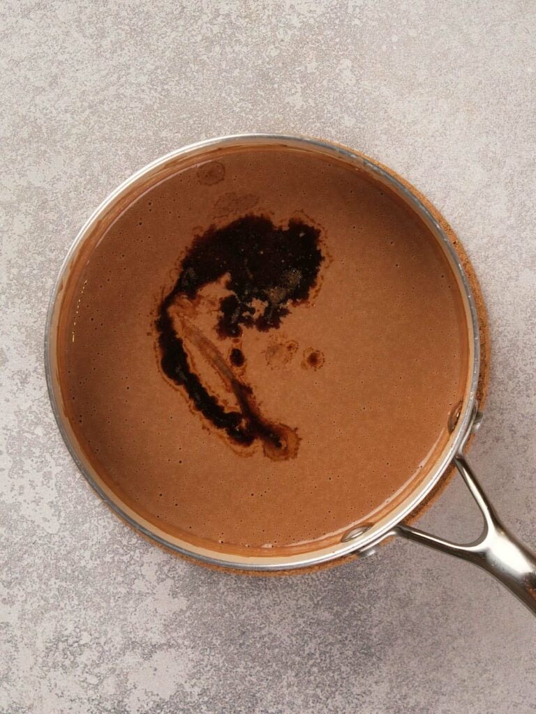 A pot with dark brown liquid, possibly chocolate sauce, on a gray surface.