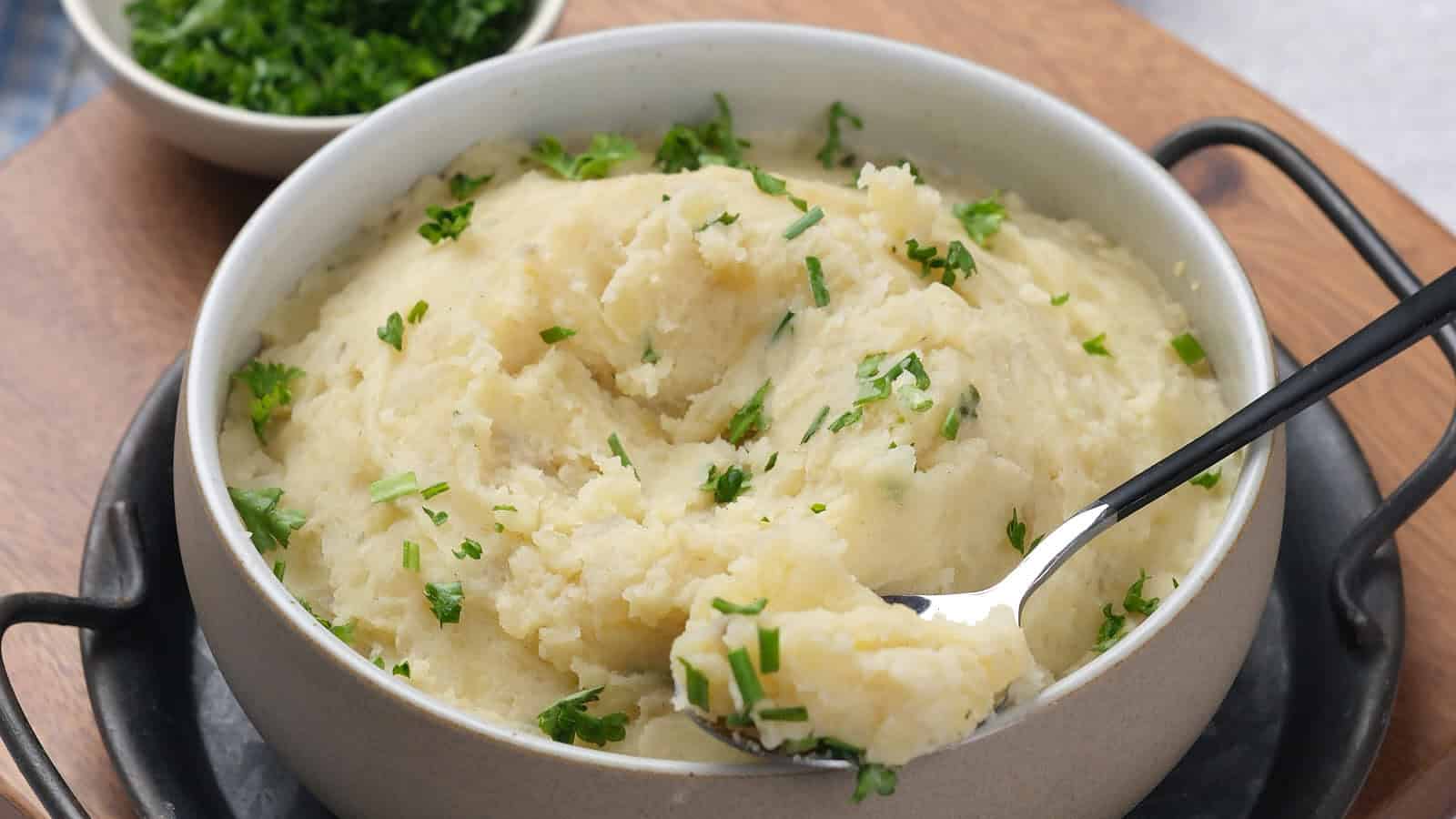 A bowl of mashed potatoes garnished with chopped parsley.