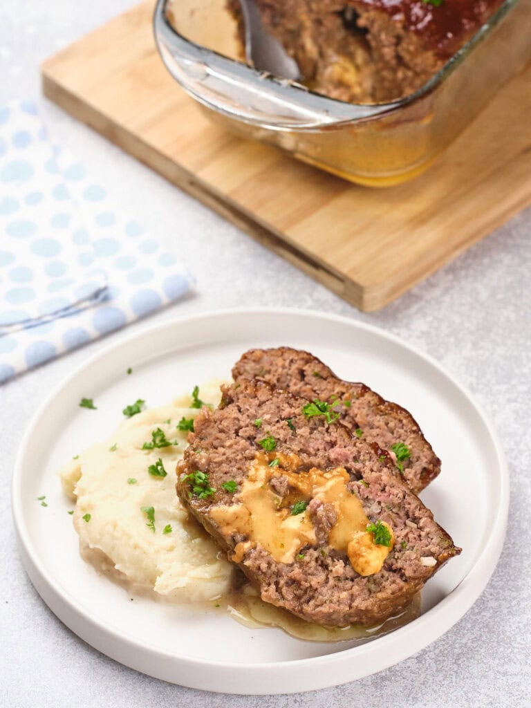 Plate with stuffed meatloaf topped with herbs, served next to mashed potatoes.