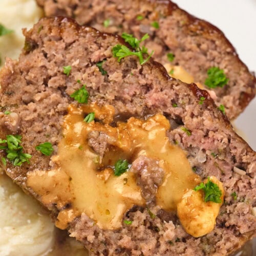 Two slices of stuffed meatloaf with melted cheese inside, garnished with parsley, served on a plate with mashed potatoes.