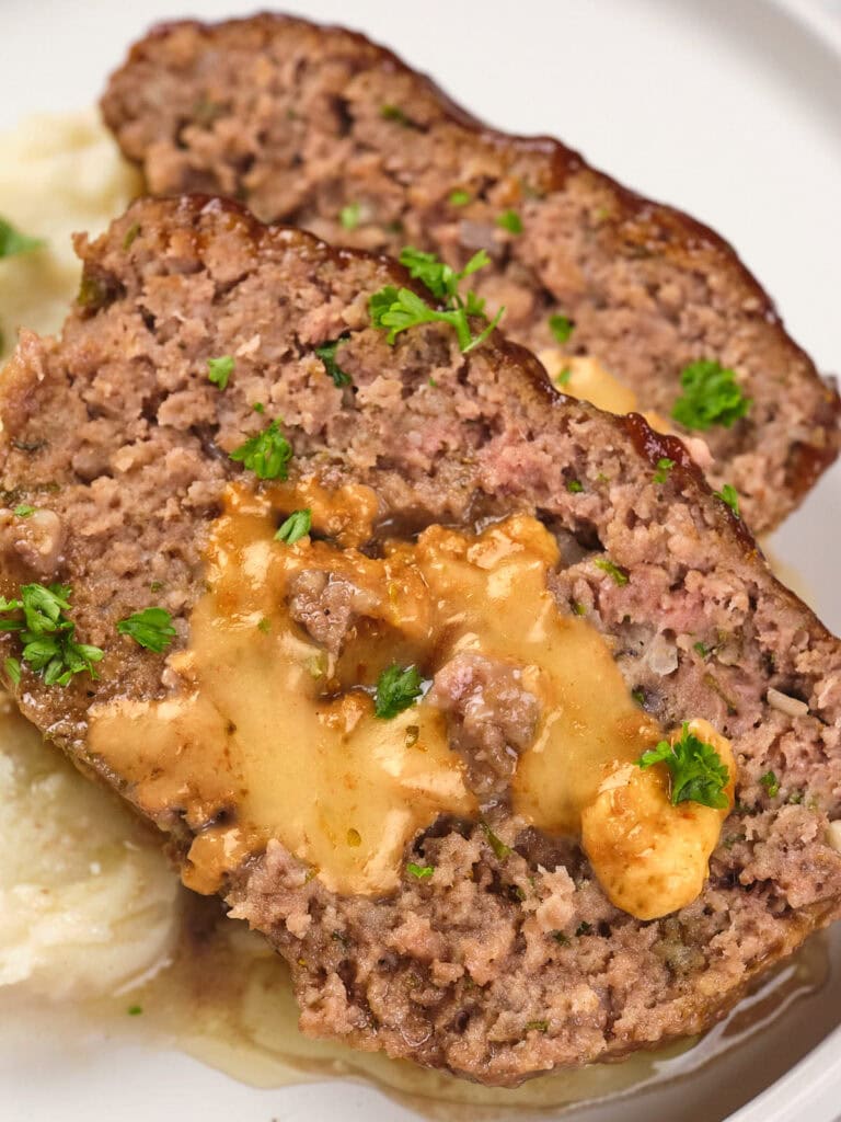 Two slices of stuffed meatloaf with melted cheese inside, garnished with parsley, served on a plate with mashed potatoes.