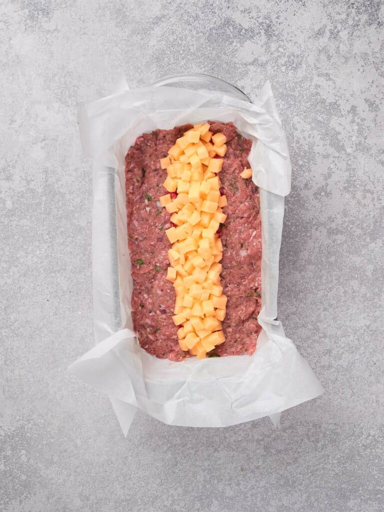 Ground meat in a parchment-lined dish with a strip of diced cheese in the center.