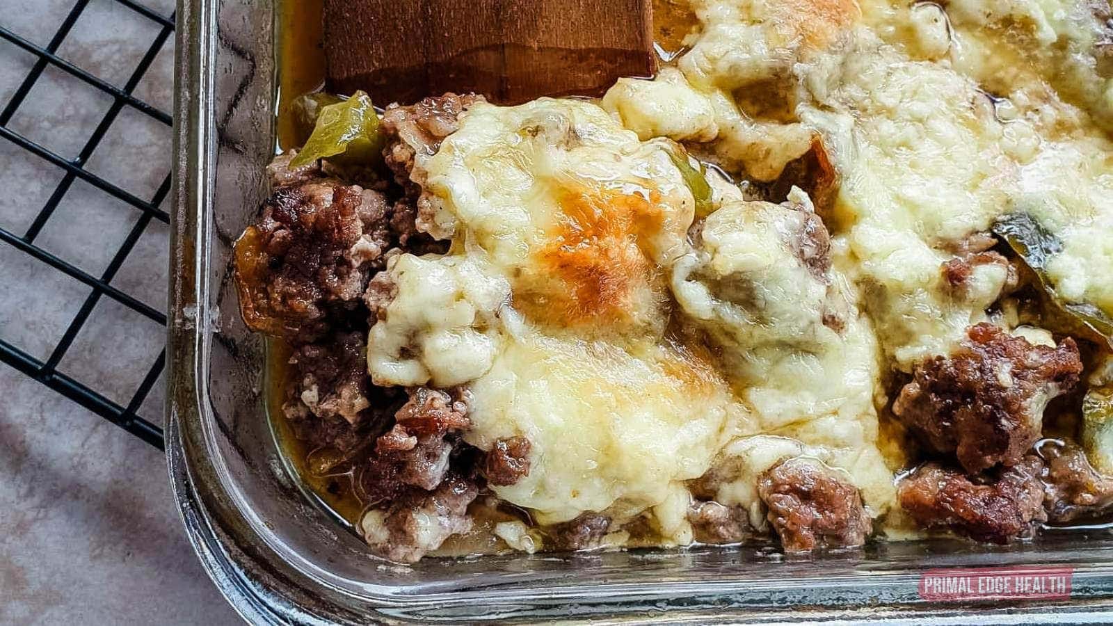 Image shows a wooden spatula cutting philly cheesesteak casserole from baking dish.