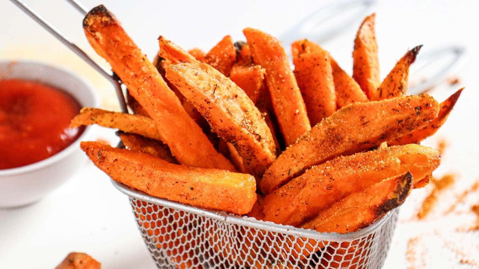 A basket of seasoned sweet potato wedges with a small bowl of ketchup beside it.