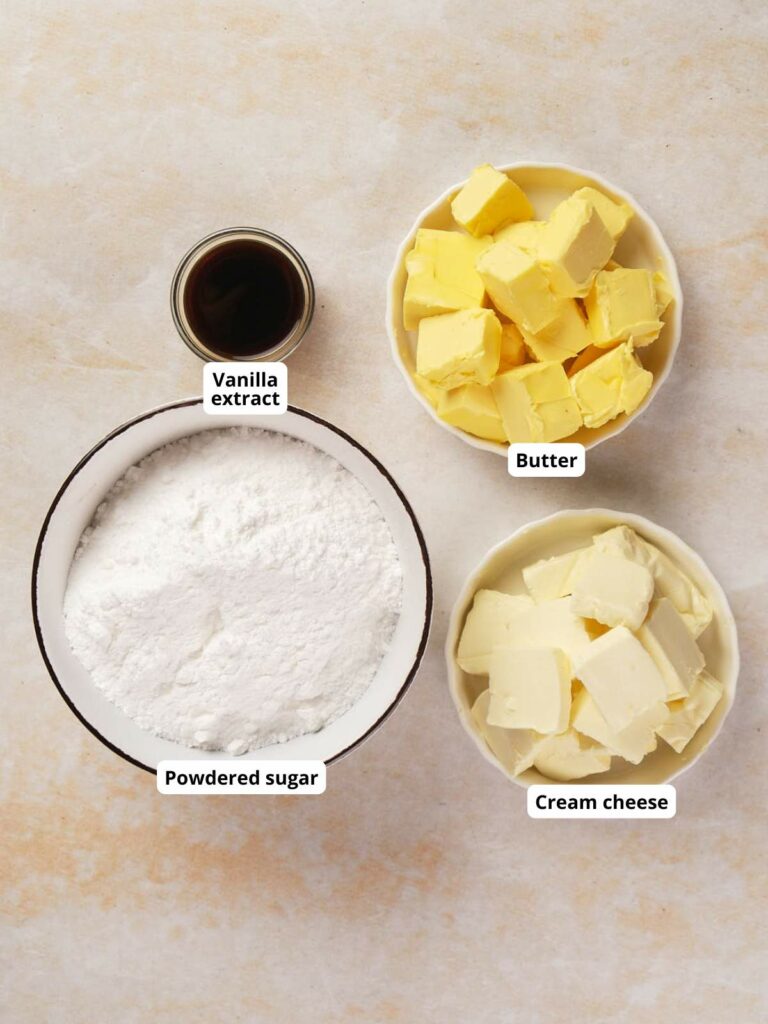 Ingredients labeled: vanilla extract, powdered sugar, butter, and cream cheese in bowls on a light surface.