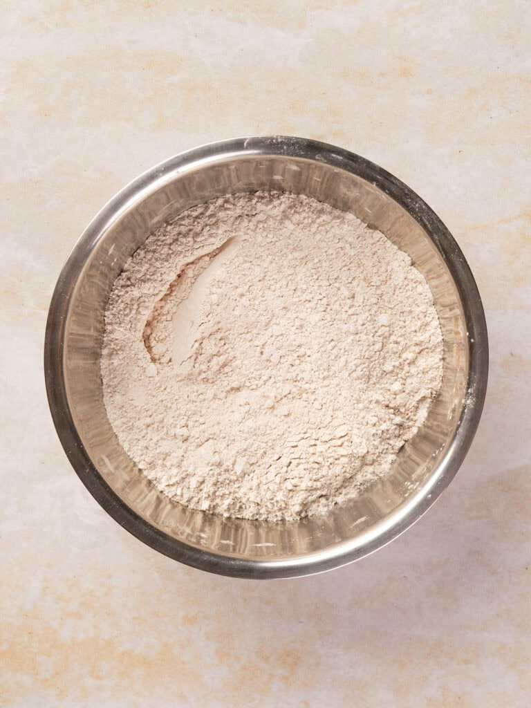 A metal bowl filled with a light beige powder, likely flour, on a neutral surface.