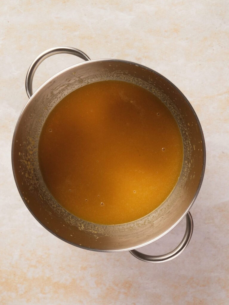 A large metal pot filled with brown broth sits on a light-colored surface.