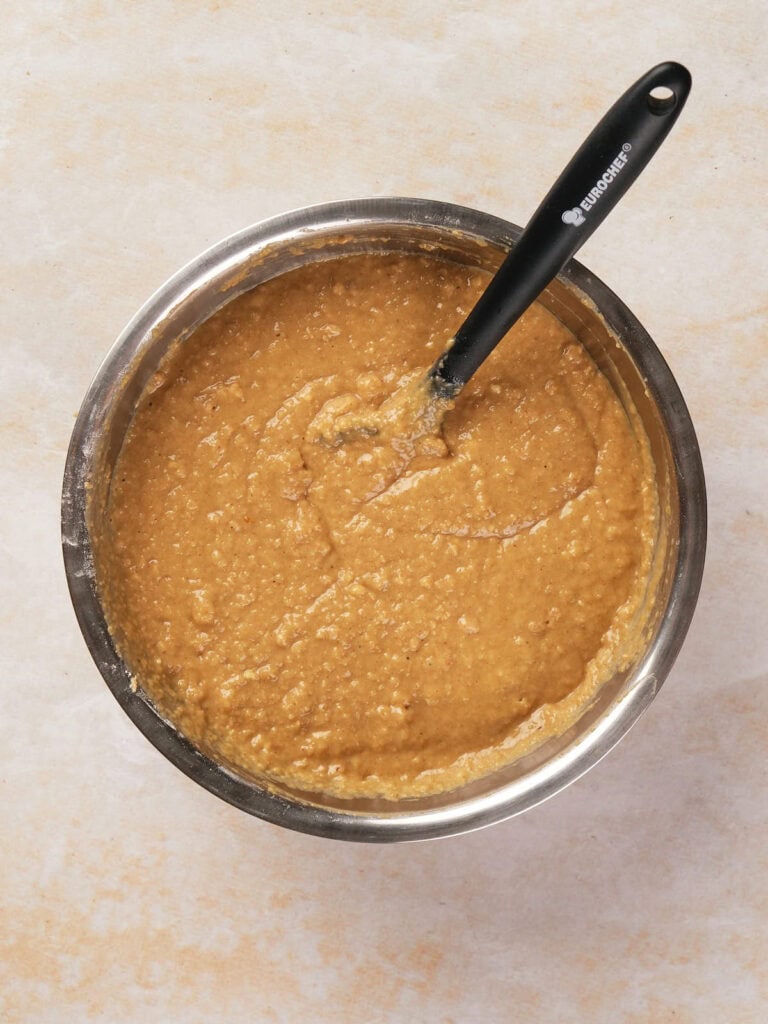 A bowl of brown batter with a black-handled spatula resting inside on a light countertop.