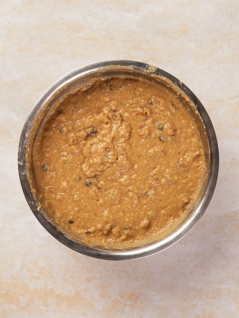 A silver bowl filled with brownish, chunky soup or stew with visible grains and small pieces.