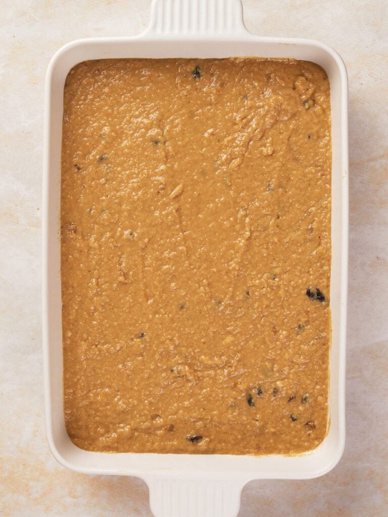 A rectangular baking dish filled with a smooth, light brown batter dotted with small dark specks.