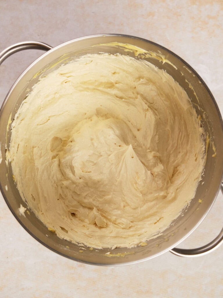 A stainless steel bowl containing creamy, light beige cake batter on a light-colored surface.