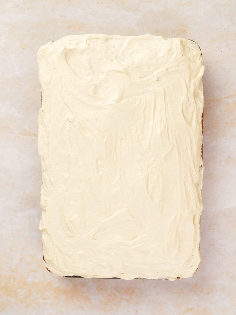 A rectangular cake topped with smooth cream frosting on a light marbled surface.