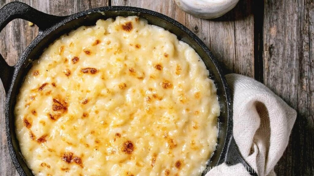 A pan of baked mac and cheese sits on a wooden surface, with a white cloth nearby.