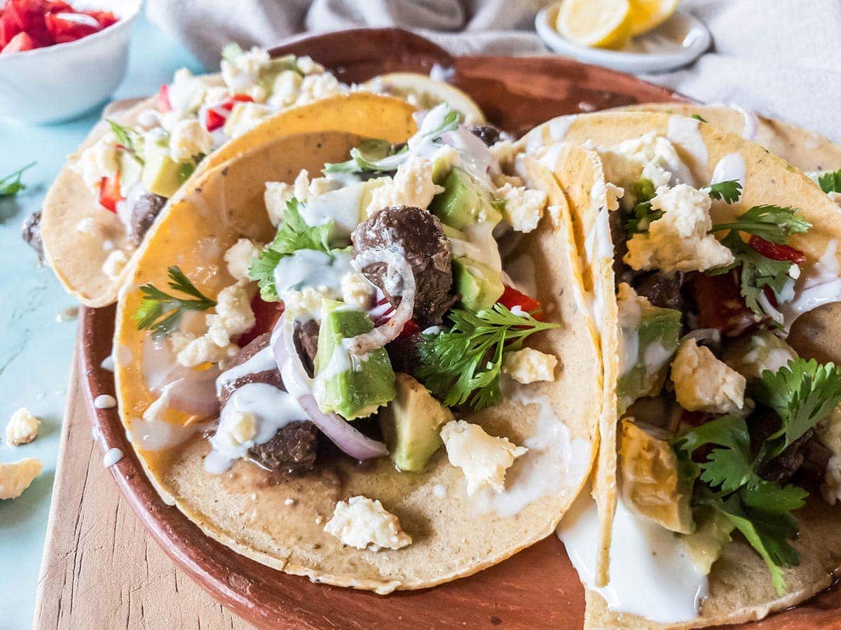 A picture of beef heart tacos with sour cream, avocado, red onion, and cilantro.