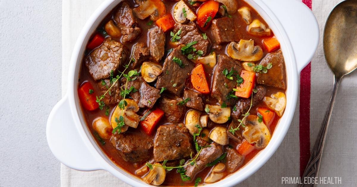 Beef stew in a white pot served with a spoon.