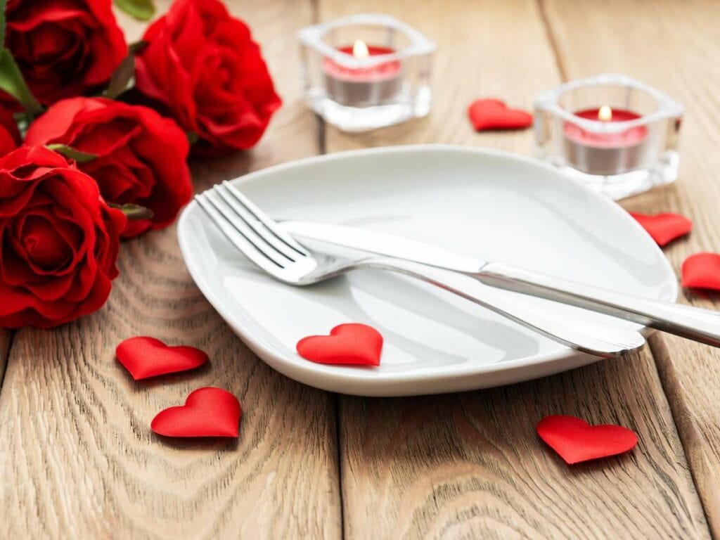 White plate with cutlery, surrounded by red roses and small heart-shaped decorations.