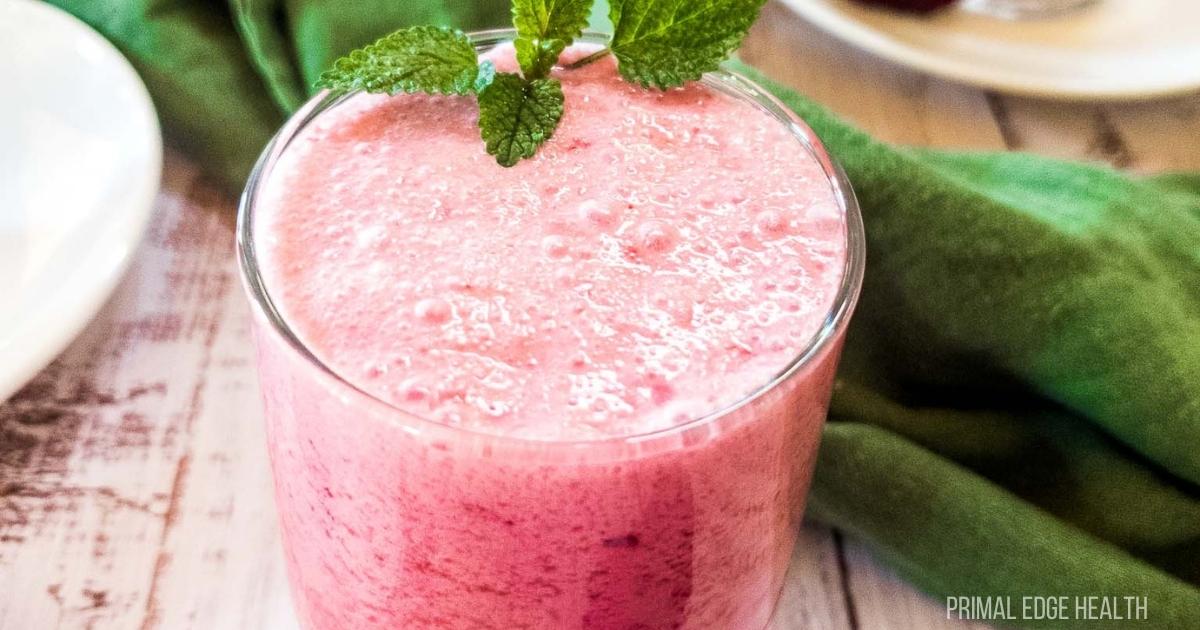 Blackberry smoothie in glass with mint garnish on white wood.