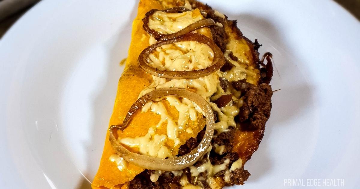 Cheeseburger omelette with ground beef on plate next to salt and pepper shakers.