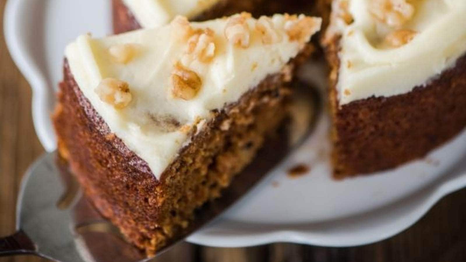 A slice of carrot cake with white frosting and walnuts, being served on a white plate.