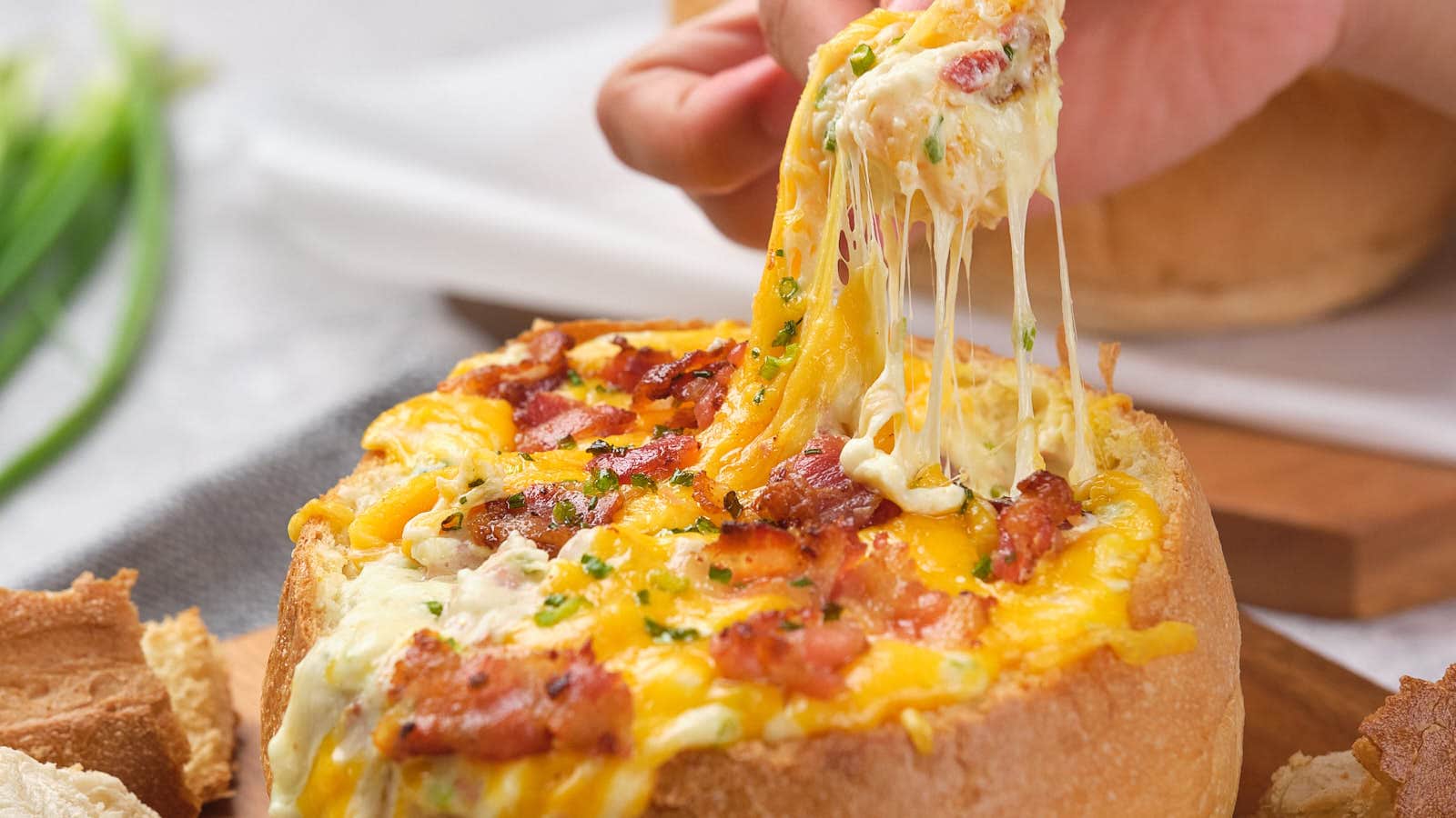 Person lifting a piece of cheese and bacon cob loaf.